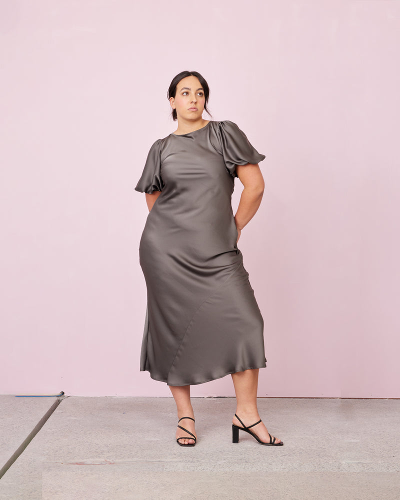 KENDALL SATIN DRESS CHARCOAL | Bias cut satin midi dress with puff sleeves and a keyhole button closure at the back neck. The bias silhouette of this dress gently contours the body, while the satin...