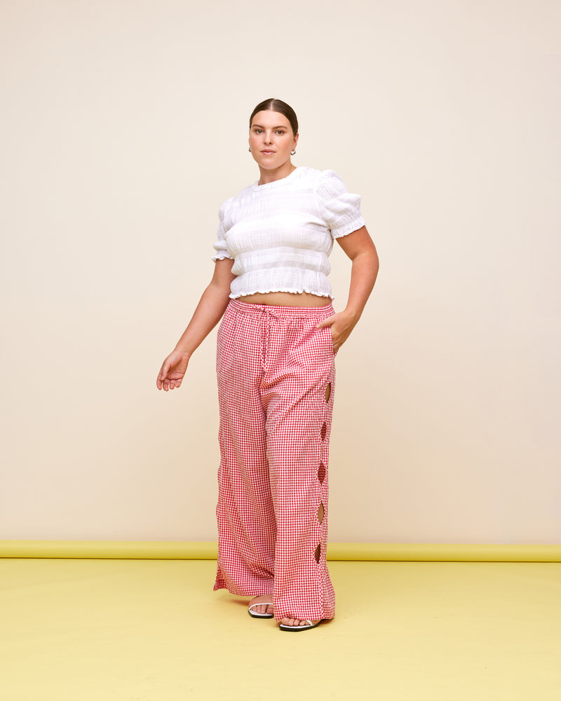 TRULLI PANT RED GINGHAM | Mid-waist cotton pant designed in a red gingham. Features wave cut-outs down the outside of the legs, making these a fun summer piece.