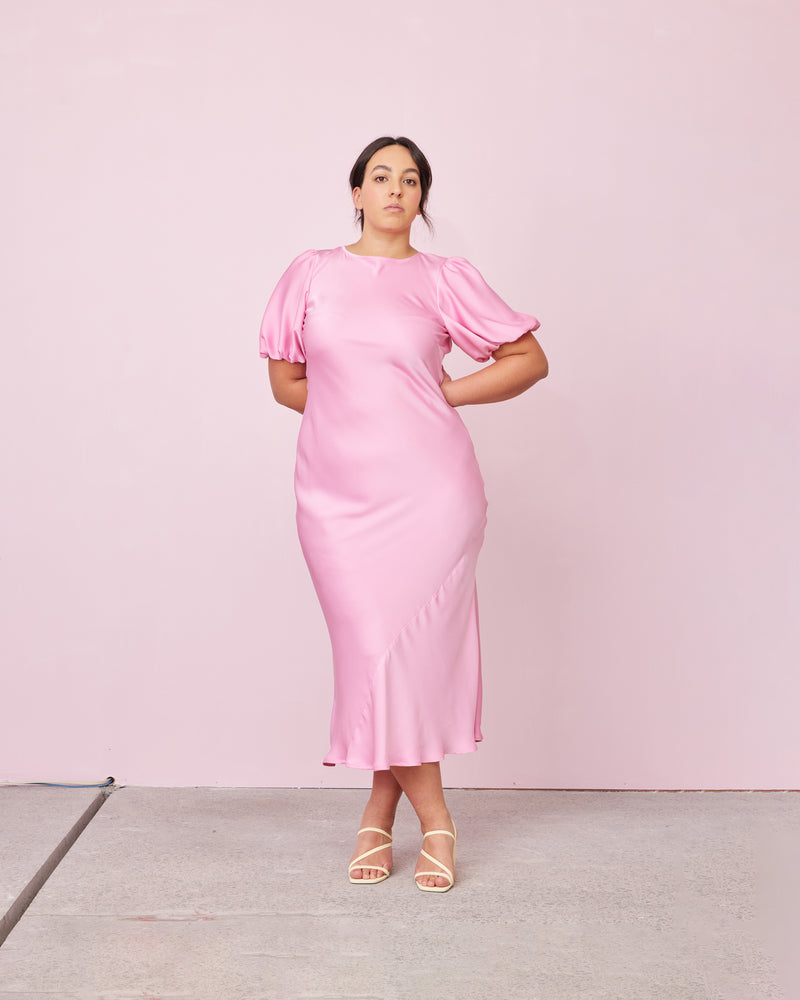 KENDALL SATIN DRESS CANDY | Bias cut satin midi dress with puff sleeves and a keyhole button closure at the back neck. The bias silhouette of this dress gently contours the body, while the satin...