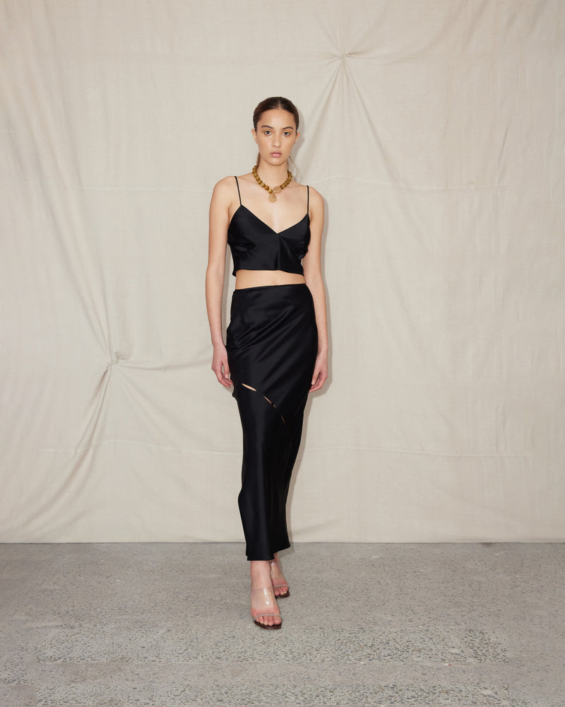 MARTY SKIRT BLACK | Maxi-length satin skirt with a side split and flat waistband. This skirt features subtle cut-outs on the bias that run down the front of the skirt, elevating this staple piece.