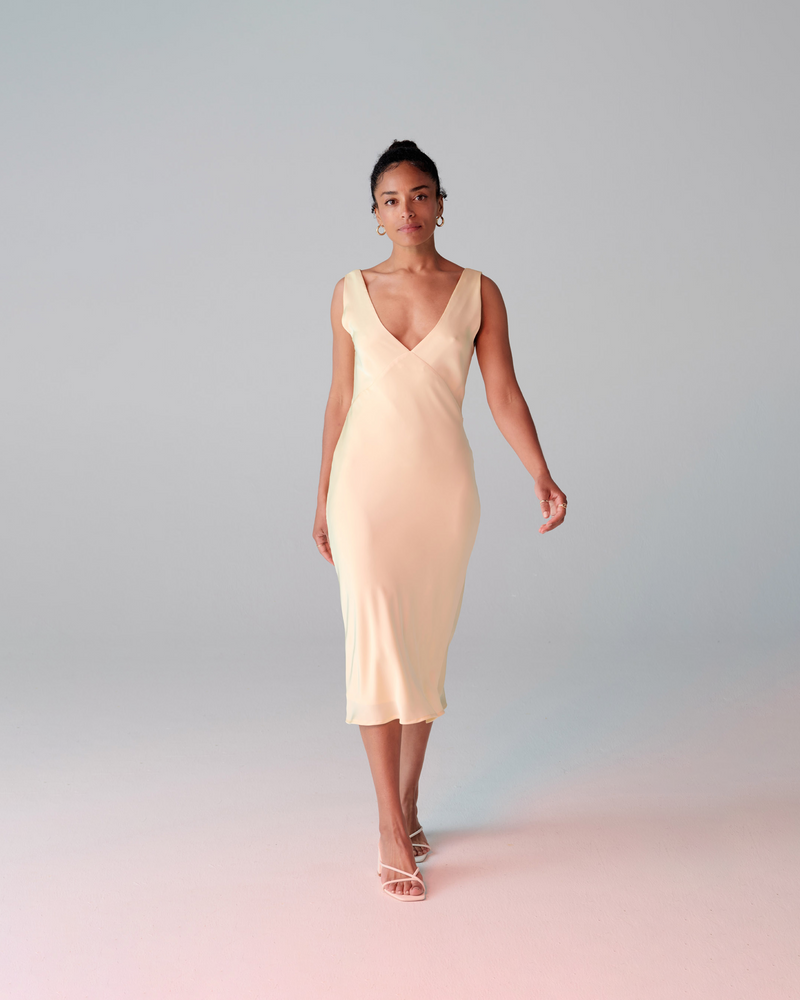 ANDIE SATIN SLIP BUTTER | Bias cut midi dress in a luxurious butter coloured satin. Wide straps and a panelled V-neck front and back give this dress a vintage shape.