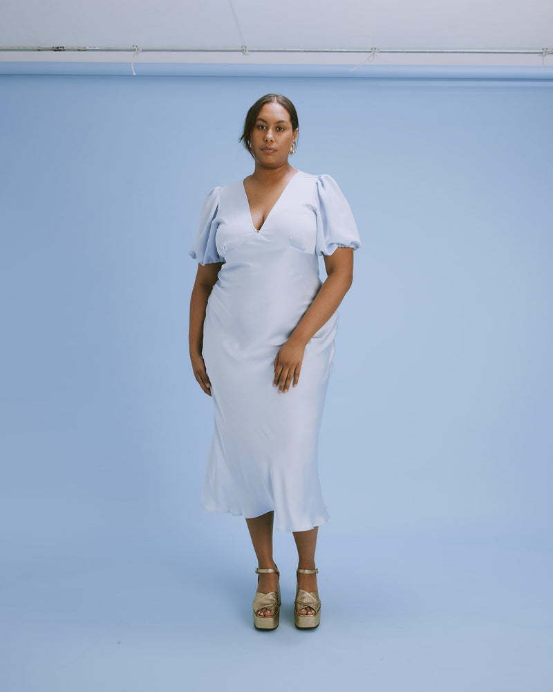 UMA SATIN DRESS ICE | Bias cut satin maxi dress with tie closure and a V-neck front and back. Back in an ice satin, with elasticated puff sleeves and ruched sleeve detailing under the bust,...