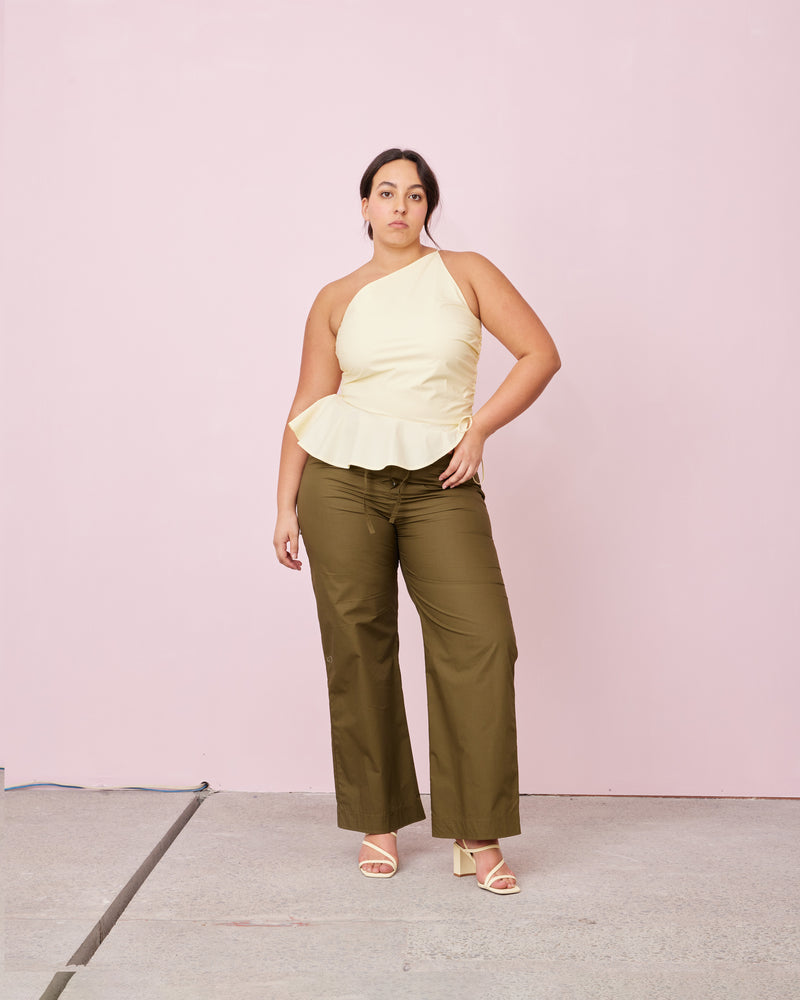 BETTINA COTTON TOP BUTTER | One shoulder cotton top with tie side gathering that can be cinched to adjust the length. The asymmetrical shape creates structure, while the peplum ruffle at the bottom hem adds...