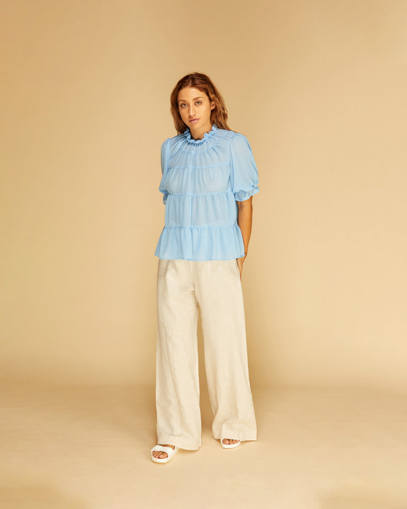 CLEMENT SHORT SLEEVE BLOUSE BLUE | Longsleeve sheer blouse with tiered details down the body. This piece has a high ruffle neckline and blouson sleeves with elasticated ruffle cuffs.