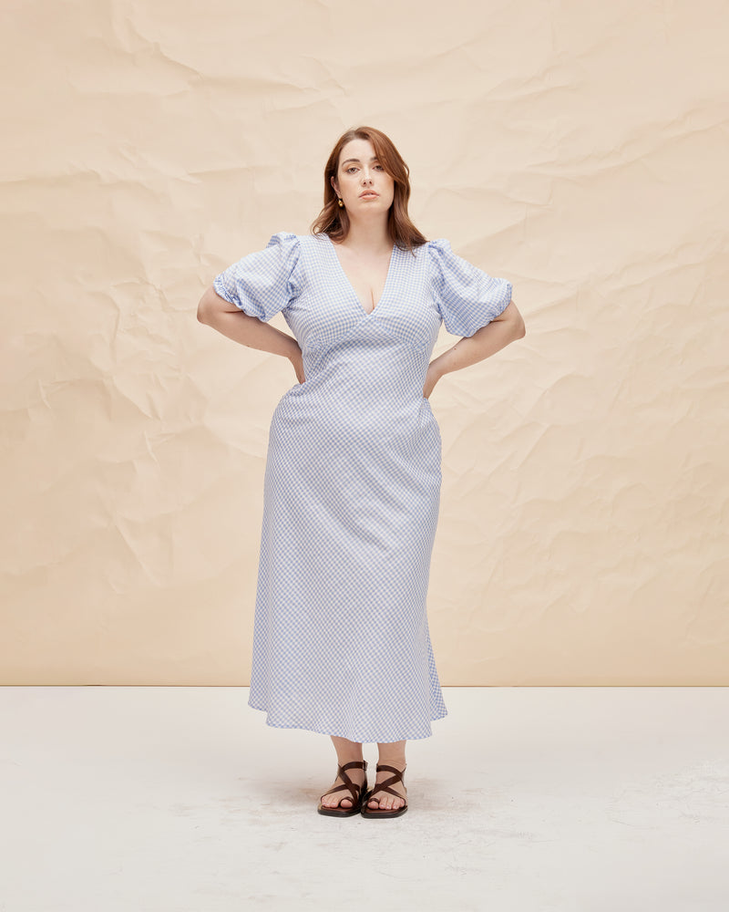 UMA DRESS BLUE GINGHAM | Bias cut cotton maxi dress with tie closure and a V-neck front and back. Back in a new blue gingham, with elasticated puff sleeves and ruched detailing under the bust, its...