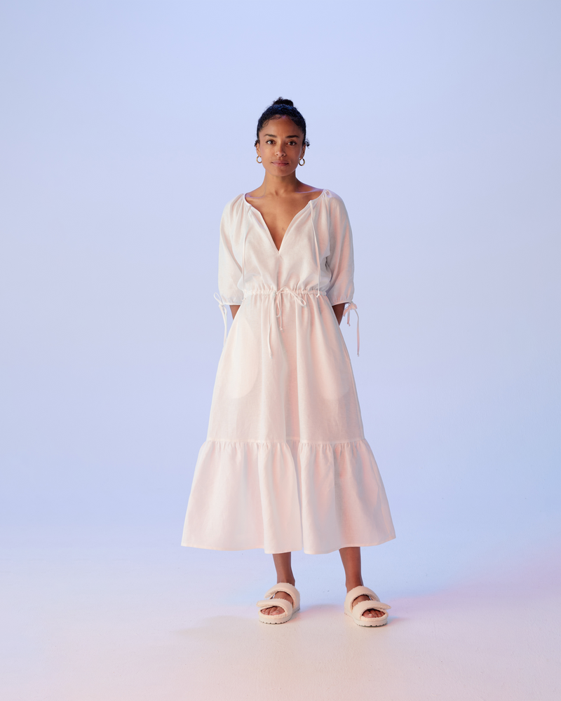 FRESH LINEN DRESS WHITE | Linen maxi dress with tie details and a gathered tier that gives this piece a gentle ruffle at the hem. The three quarter length sleeves, neckline and waist are finished...