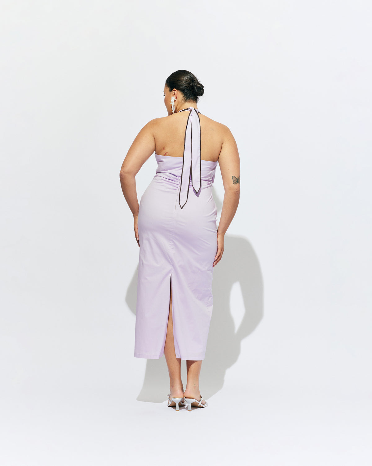 JOEY DRESS LILAC | Bias cut midi dress with a tie-up halter neckline, crafted in our lilac organic cotton. Designed with ruching details on the waist and back for a tailored fit through the body, which falls into a straight cut skirt with a...