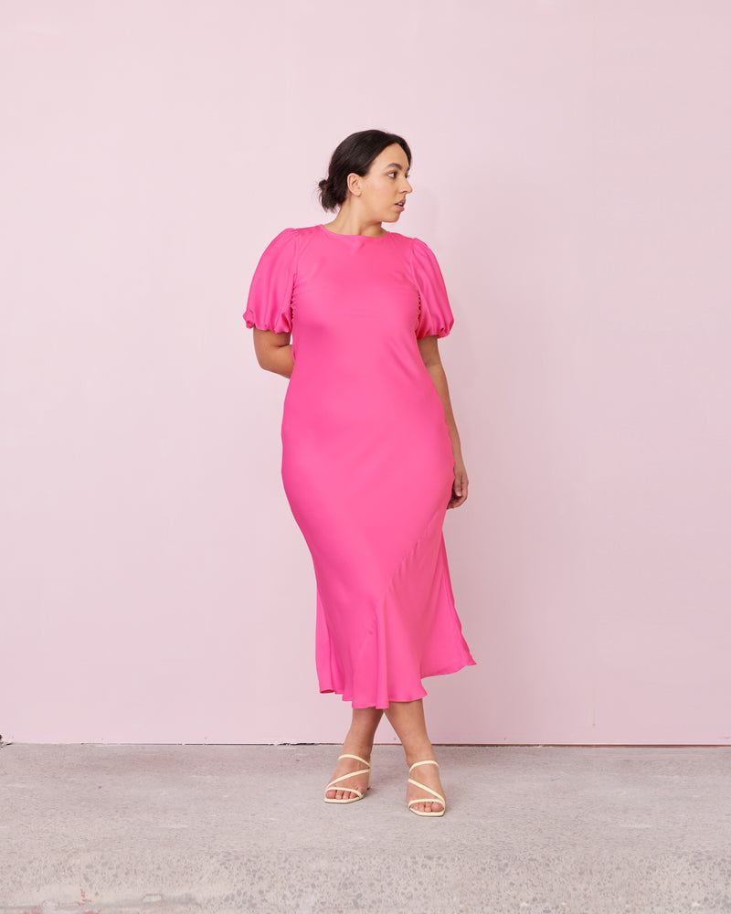 KENDALL SATIN DRESS HOT PINK | Bias cut satin midi dress with puff sleeves and a keyhole button closure at the back neck. The bias silhouette of this dress gently contours the body, while the satin...