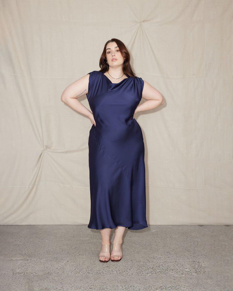  CURTIS MIDI DRESS MULHOLLAND NAVY | Bias cut cap sleeve midi dress crafted in a luxe Mulholland navy satin. This piece has ruched detail at the shoulder, a tie to cinch in the waist, and a...