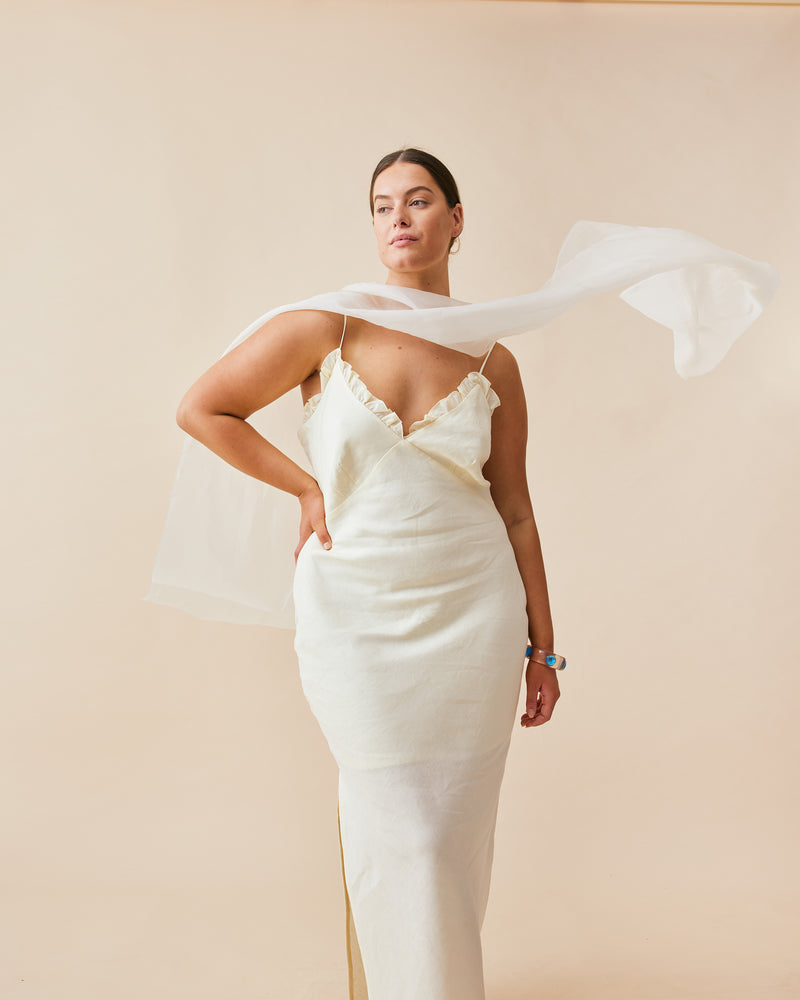 DELILAH LINEN SLIP BUTTER | Bias cut slip with a V-neckline, with ruffle detailing around the bust line, designed in a butter colour. This slip features bust shaping and a side split on one side,...