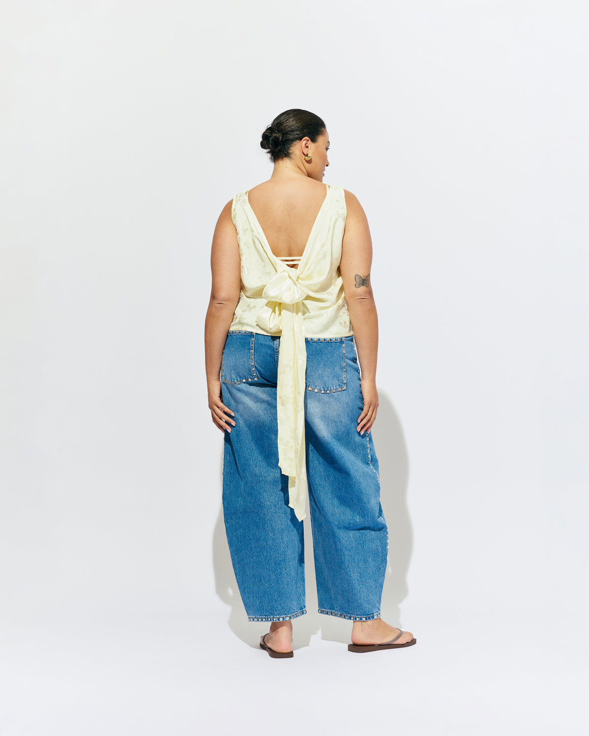 LIZ TOP BUTTER JACQUARD | Liz is a relaxed fit sleeveless top with a wrap feature, accentuated with long waist ties that can be tied around the body or at the back in a bow. Imagined in a sheeny jacquard satin, when this fabric catches...