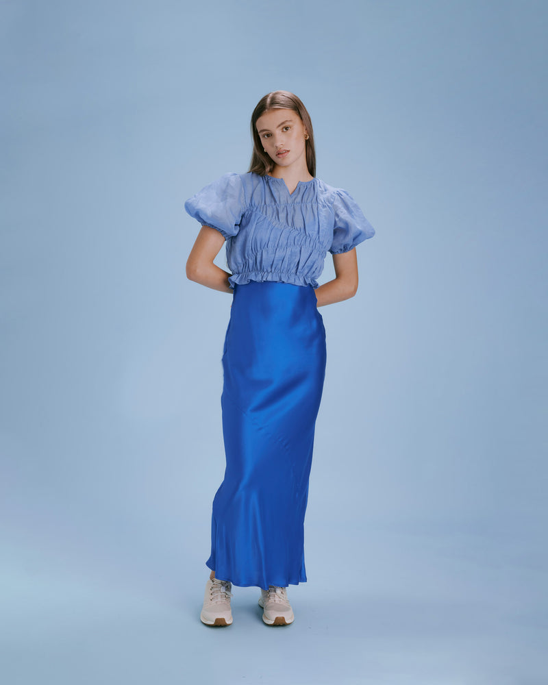 LILLIE TOP BLUE IRIS | Elasticated crop blouse with puff sleeves and a frill hem, made from a delicate translucent ramie voile. The elastic detail creates texture in the piece, and contrasts with the gauzy...