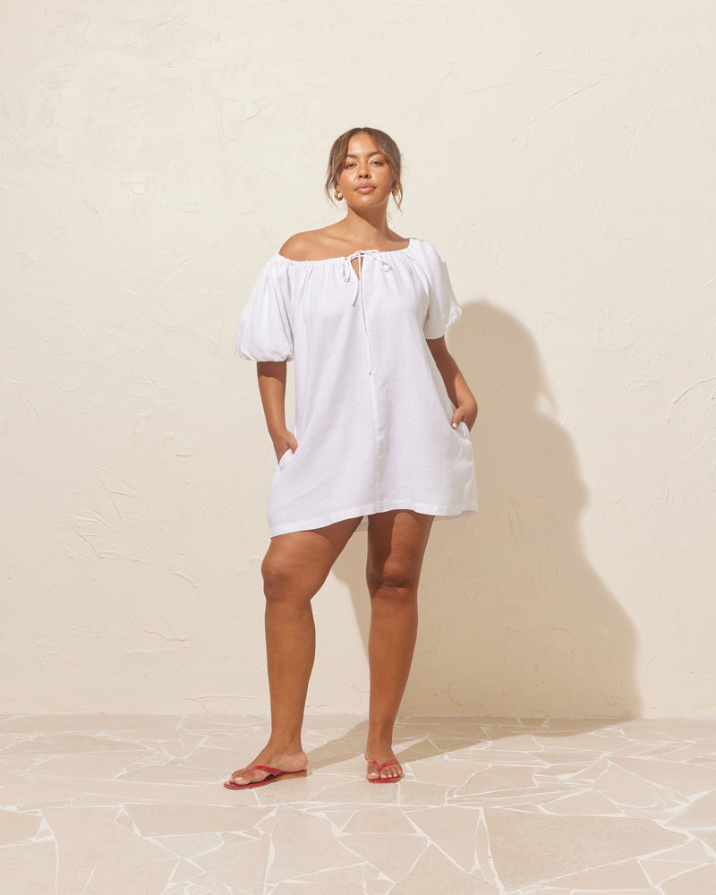 FLORY MINI DRESS WHITE | Short sleeve mini dress designed with a gathered neckline that ties at the centre front. Made from a soft linen blend, this dress can be worn on or off the...