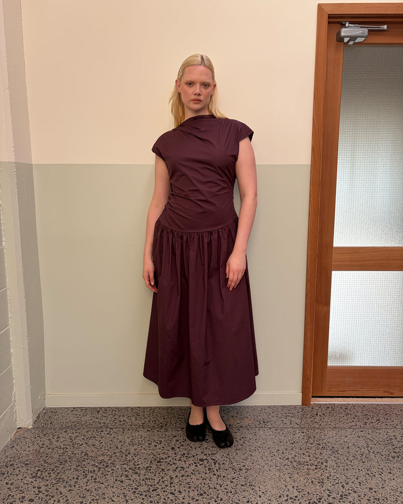 BIRDIE MAXI DRESS BURGUNDY | Drop waist maxi dress designed in a burgundy organic cotton. Featuring a high neck collar, pleated skirt and a gather detail on the lower back designed for better fit and movement. Layer with your favourite knitwear or our Coco Blazer...