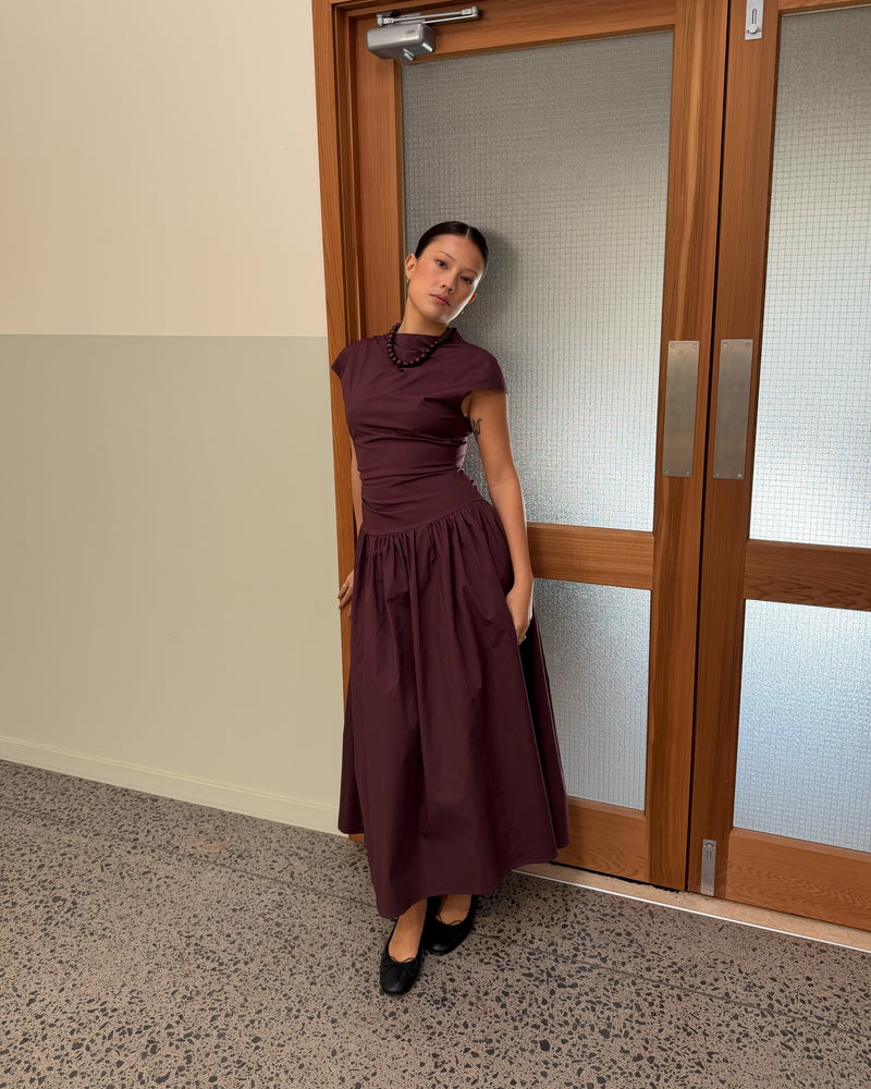 BIRDIE MAXI DRESS BURGUNDY | Drop waist maxi dress designed in a burgundy organic cotton. Featuring a high neck collar, pleated skirt and a gather detail on the lower back designed for better fit and movement. Layer with your favourite knitwear or our Coco Blazer...