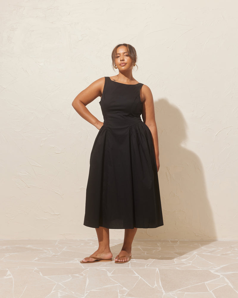 CARMELA BOW DRESS BLACK | Sleeveless midi dress with a high, boat neckline, designed in an organic cotton. This dress has a floaty A-line skirt and turns to reveal an oversized bow at the back.