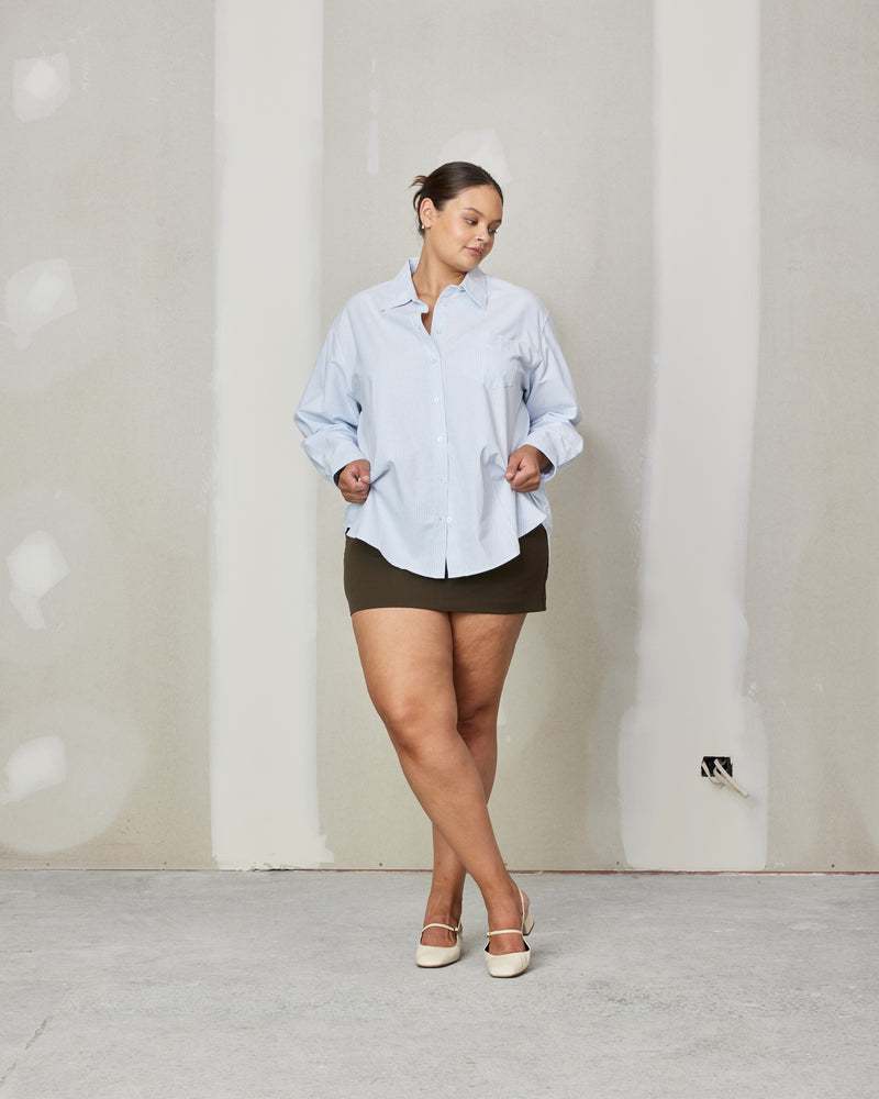 ALLORA SHIRT BLUE STRIPE | Oversized crisp shirt with classic shirt detailing and a large front pocket, designed in a blue striped cotton. This piece is a timeless wardrobe staple that you will wear for...