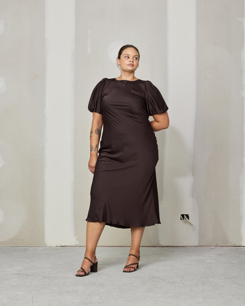KENDALL SATIN  DRESS ESPRESSO | Bias cut satin midi dress with puff sleeves and a keyhole button closure at the back neck. The bias silhouette of this dress gently contours the body, while the espresso...
