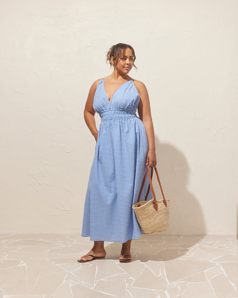 HERO MAXI DRESS BLUE GINGHAM | Double strap maxi dress with a plunge neckline, shirred waist detail, and side split in an organic blue gingham cotton. The shirring at the waist accentuates the full skirt.