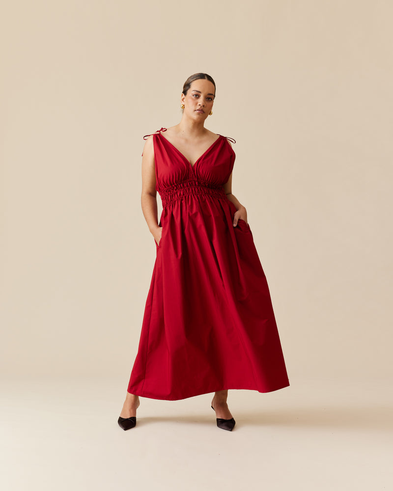 HERO MAXI DRESS GARNET | Double strap maxi dress with a plunge neckline, shirred waist detail, and side split in a garnet red cotton. The shirring at the waist accentuates the full skirt.
