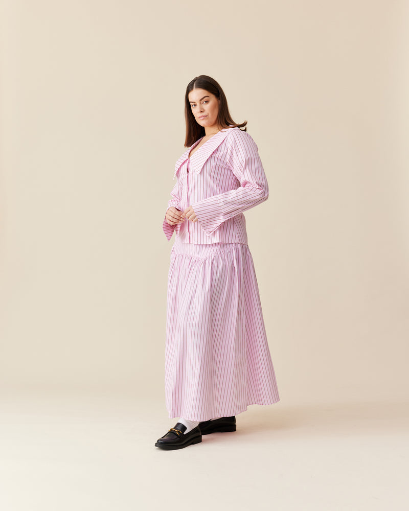 TRULLI SKIRT PINK RED STRIPE | Floaty basque style maxi skirt imagined in a pink striped cotton. This skirt features an asymmetrical bodice-style waistline, that falls to a full, wide skirt.
