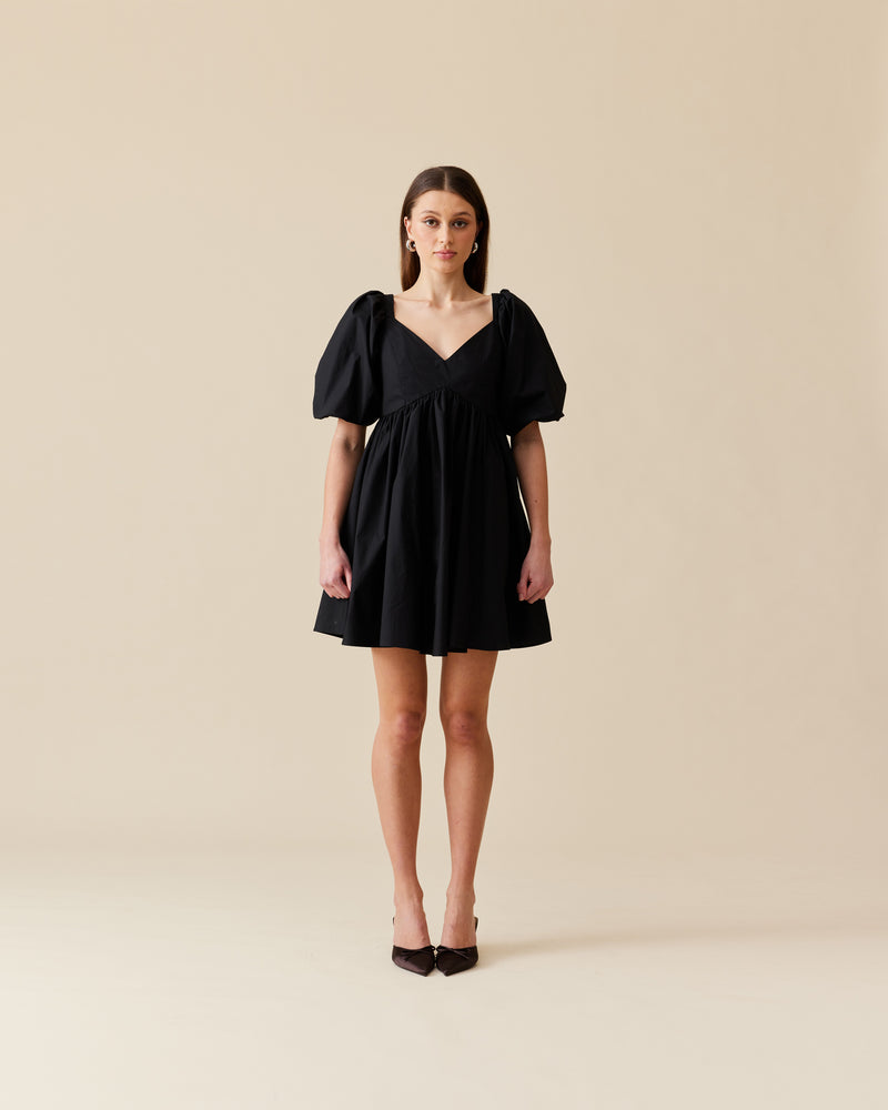 NONI MINI DRESS BLACK | Baby doll mini dress crafted in a black cotton. Features panelling at the bust that falls to a soft, A-line gathered skirt and puff sleeves.
