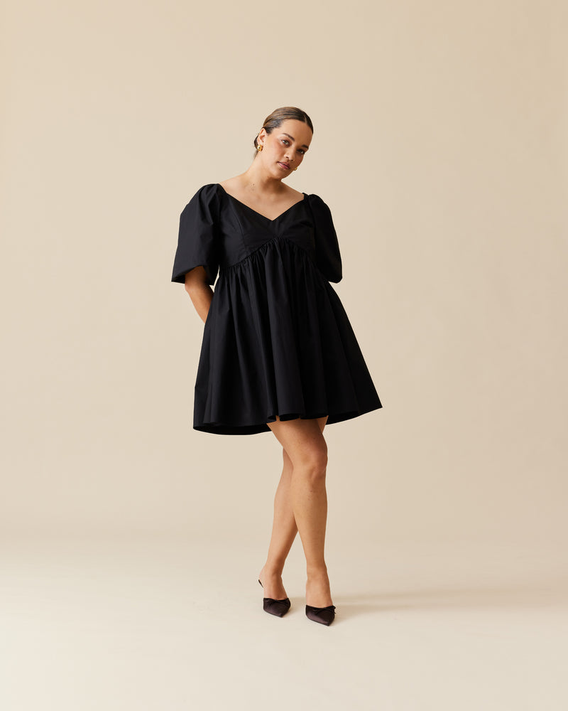 NONI MINI DRESS BLACK | Baby doll mini dress crafted in a black cotton. Features panelling at the bust that falls to a soft, A-line gathered skirt and puff sleeves.
