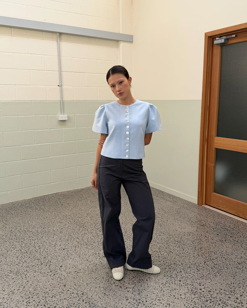 CAROLYN SHORT SLEEVE BLAZER LIGHT BLUE | Collarless short sleeve light blue blazer with feature pearlescent buttons. An elevated classic with a structured silhouette, this top is the perfect addition to your everyday workwear rotation. Pair with your favourite trousers, or denim for a more casual look.
