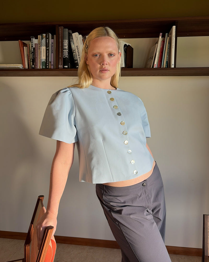 CAROLYN SHORT SLEEVE BLAZER LIGHT BLUE | Collarless short sleeve light blue blazer with feature pearlescent buttons. An elevated classic with a structured silhouette, this top is the perfect addition to your everyday workwear rotation. Pair with your favourite trousers, or denim for a more casual look.