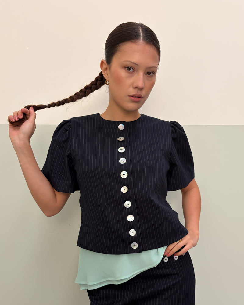 CAROLYN SHORT SLEEVE BLAZER NAVY PINSTRIPE | Collarless short sleeve espresso blazer with feature pearlescent buttons. An elevated classic with a structured silhouette, this top is the perfect addition to your everyday workwear rotation. Pair with the Carolyn Pant for a full suiting moment. 