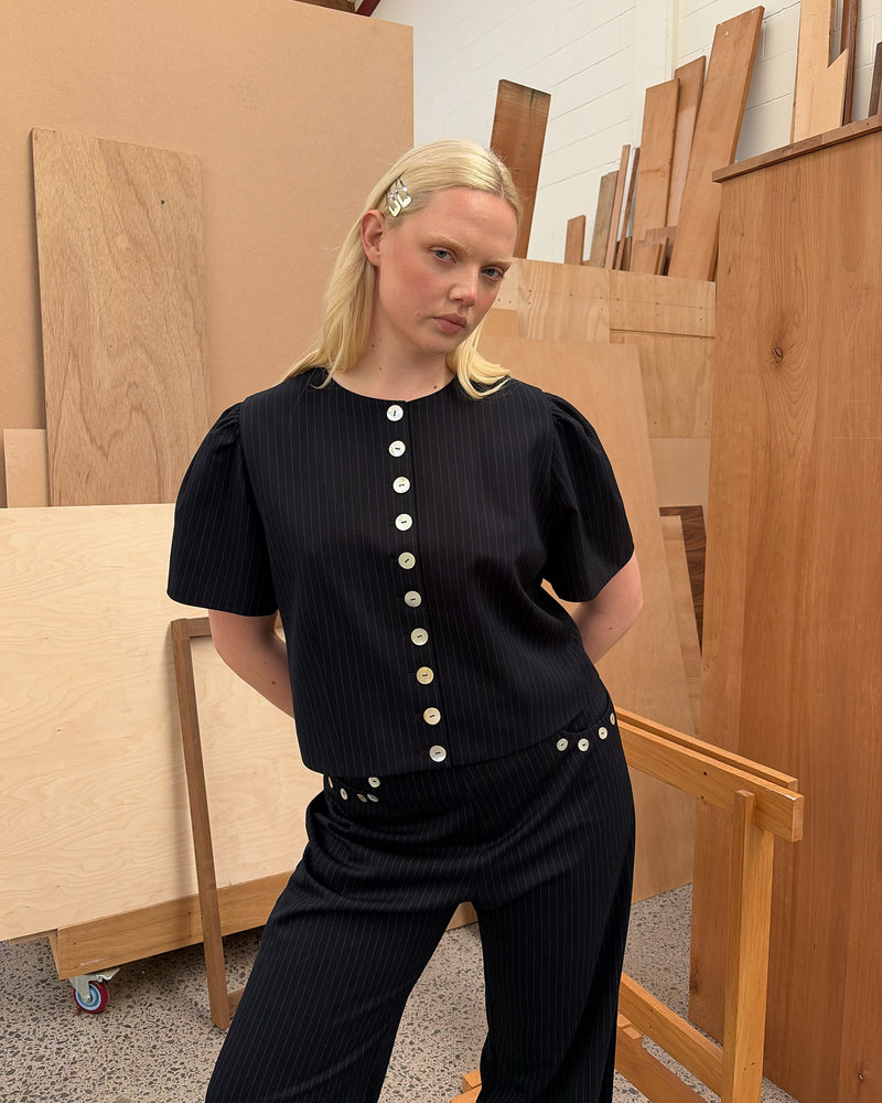 CAROLYN SHORT SLEEVE BLAZER NAVY PINSTRIPE | Collarless short sleeve espresso blazer with feature pearlescent buttons. An elevated classic with a structured silhouette, this top is the perfect addition to your everyday workwear rotation. Pair with the Carolyn Pant for a full suiting moment. 