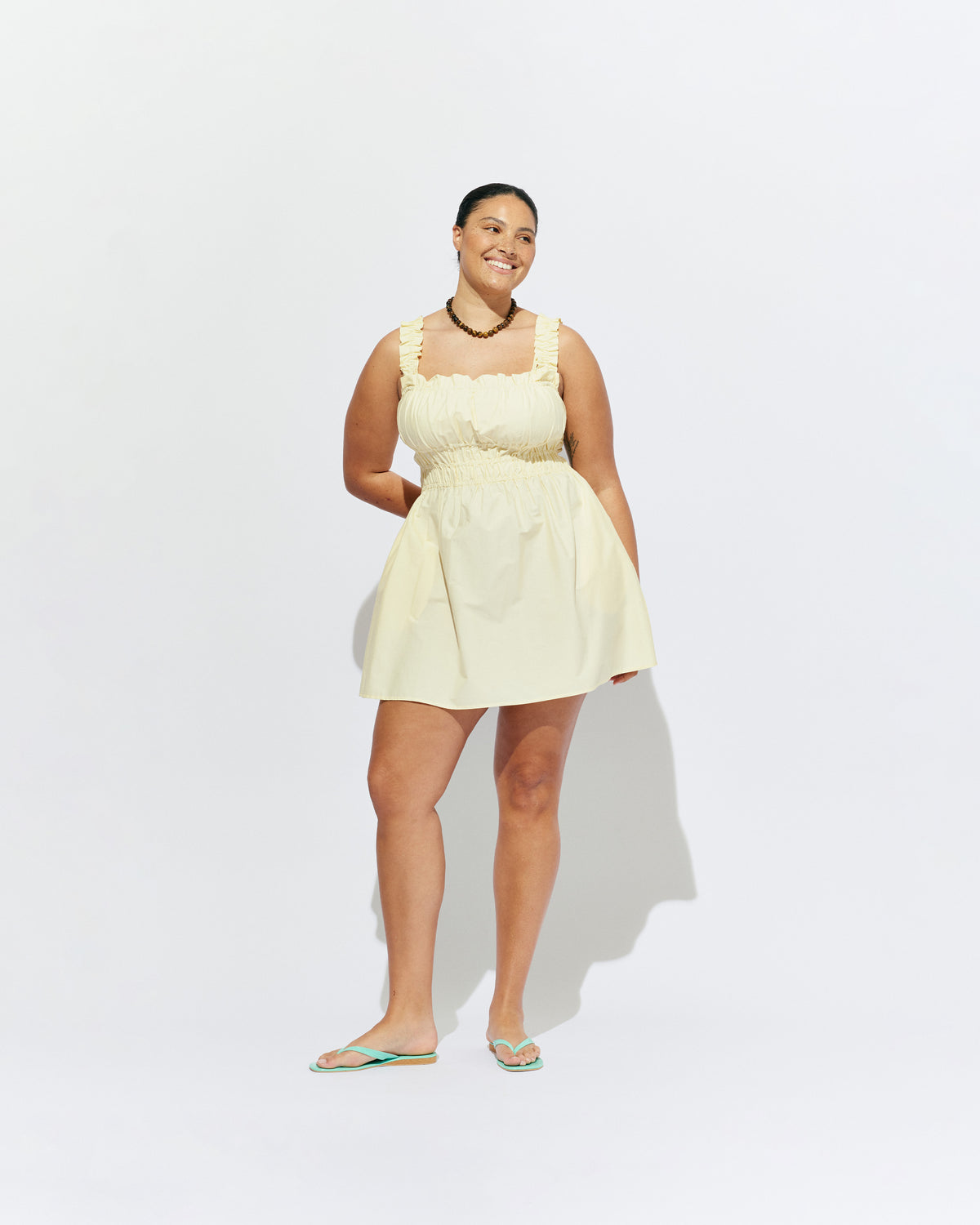 TRULLI RUCHED MINI DRESS BUTTER | Sleeveless cotton mini dress designed in a butter yellow organic cotton, with a square neckline and shirred bodice and straps. This dress falls to an A-line skirt, that features pockets to house all your essentials.