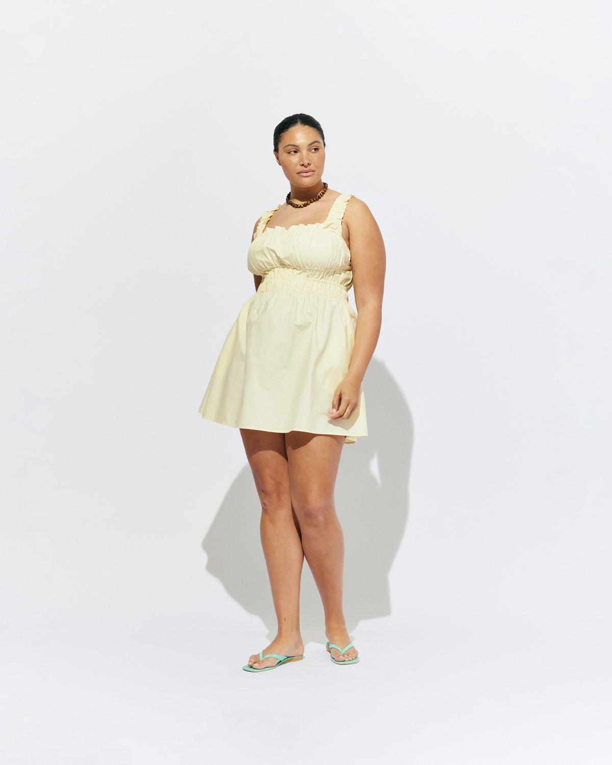 TRULLI RUCHED MINI DRESS BUTTER | Sleeveless cotton mini dress designed in a butter yellow organic cotton, with a square neckline and shirred bodice and straps. This dress falls to an A-line skirt, that features pockets to house all your essentials.