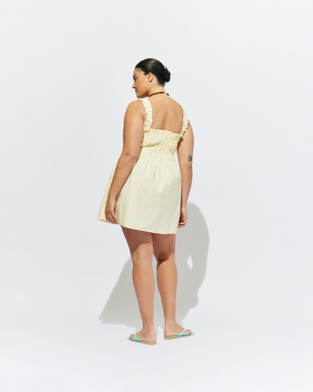 TRULLI RUCHED MINI DRESS BUTTER | Sleeveless cotton mini dress designed in a butter yellow organic cotton, with a square neckline and shirred bodice and straps. This dress falls to an A-line skirt, that features pockets to house all your essentials.