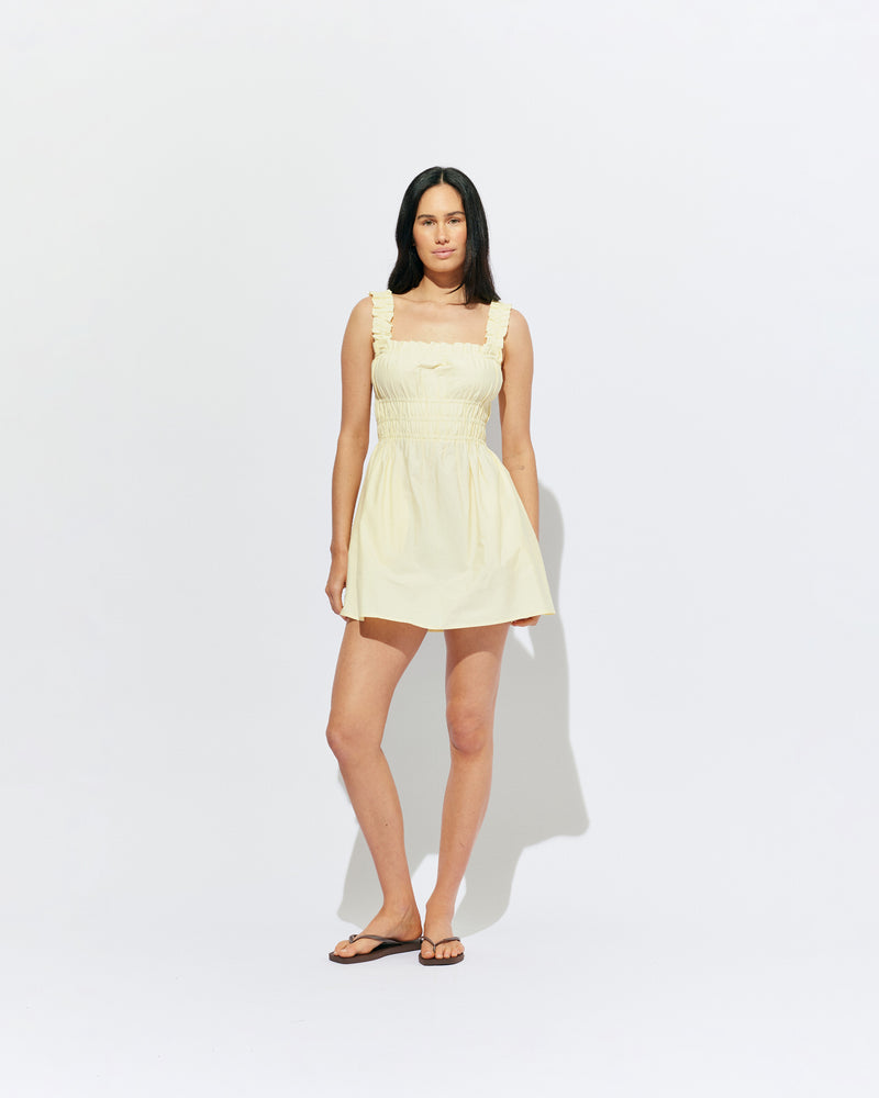 TRULLI RUCHED MINI DRESS BUTTER | Sleeveless cotton mini dress designed in a butter yellow organic cotton, with a square neckline and shirred bodice and straps. This dress falls to an A-line skirt, that features pockets to house all your essentials.