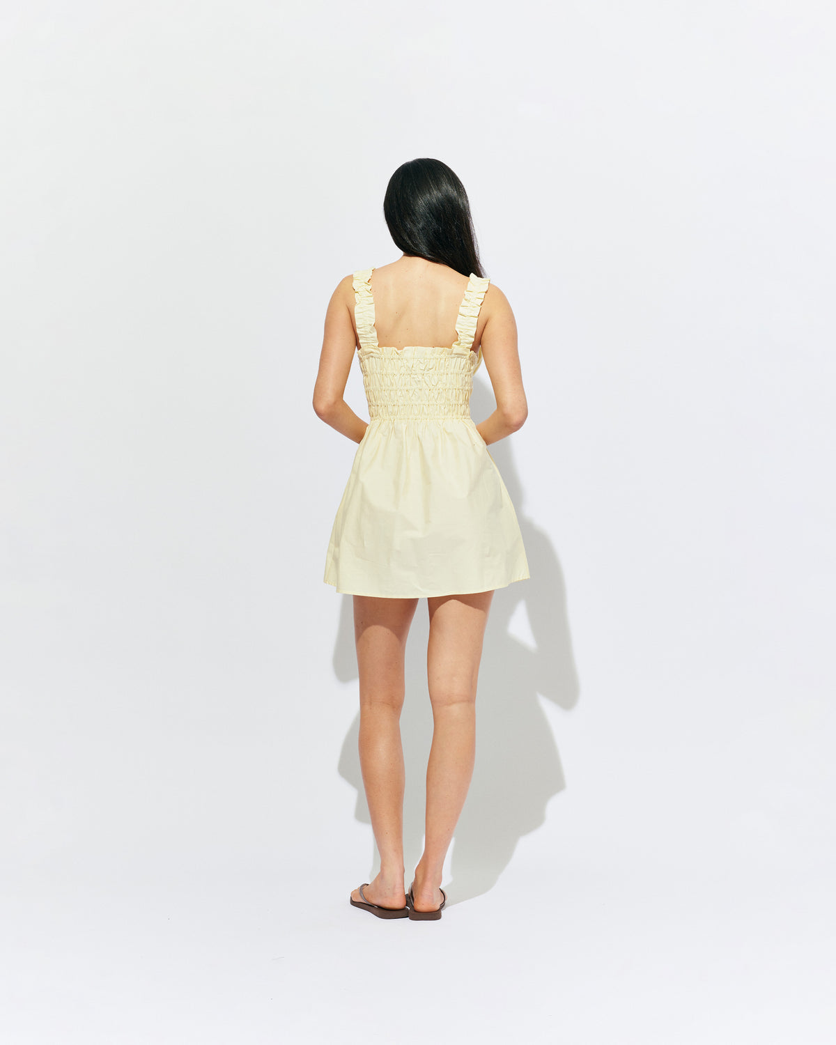 TRULLI RUCHED MINI DRESS BUTTER | Sleeveless cotton mini dress designed in a butter yellow organic cotton, with a square neckline and shirred bodice and straps. This dress falls to an A-line skirt, that features pockets to house all your essentials.