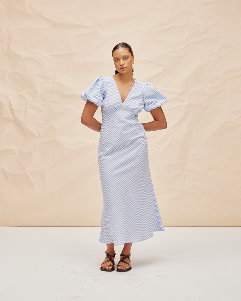 UMA DRESS BLUE GINGHAM | Bias cut cotton maxi dress with tie closure and a V-neck front and back. Back in a new blue gingham, with elasticated puff sleeves and ruched detailing under the bust, its...