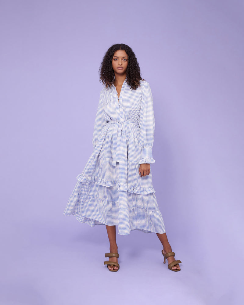 VAL GINGHAM DRESS BLUE GINGHAM | Tiered shirt style maxi dress with frilled cuff and collar detail and a waist tie belt, designed in a blue gingham with hints of pink throughout. Tiered ruching throughout the...