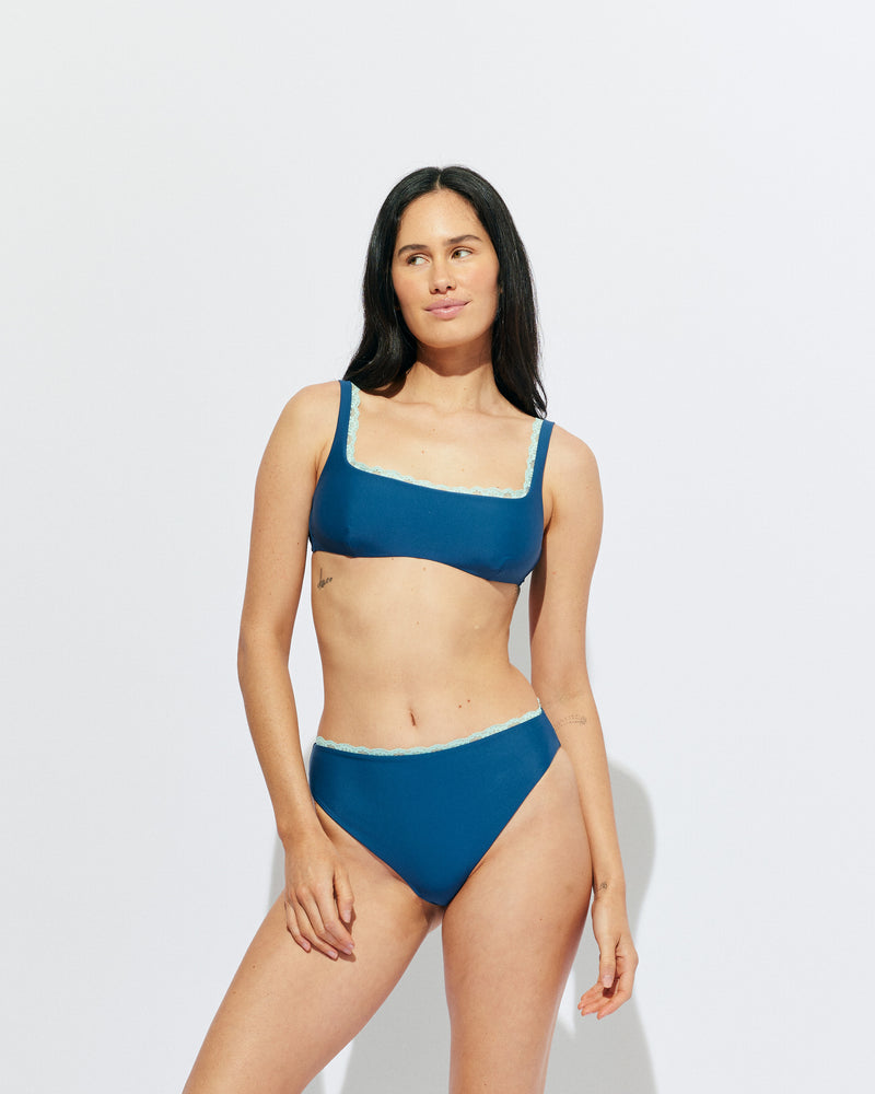 WYLIE BIKINI TANK TOP NAVY | Named after the Wylie's Baths in Sydney, this navy scoop neck bikini top is designed for higher coverage and support with a peek of aqua lace trim along the bust. With an adjustable back tie and straps for a flexible...